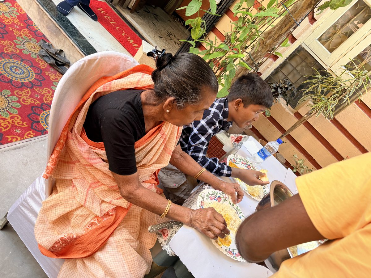 Woman in orange sari helping a child with ceremonial activity on the mat
