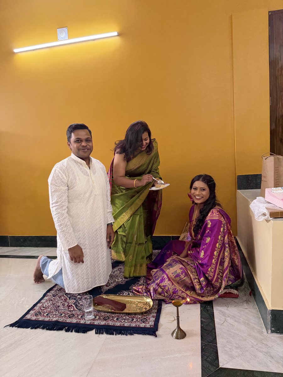 Man kneeling as woman in gold offers blessings, Rituparna seated nearby