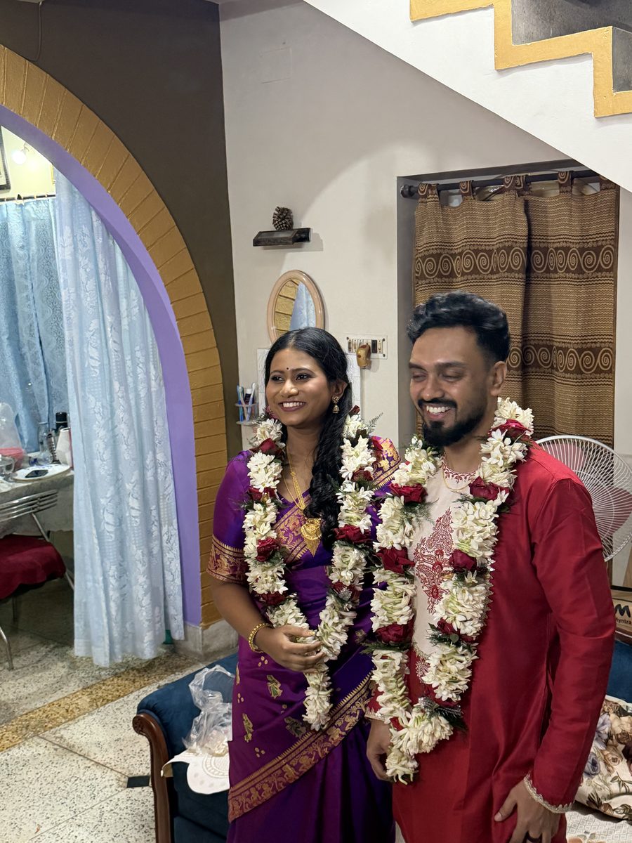 Rituparna and Shoumo wearing flower garlands, smiling together near a window