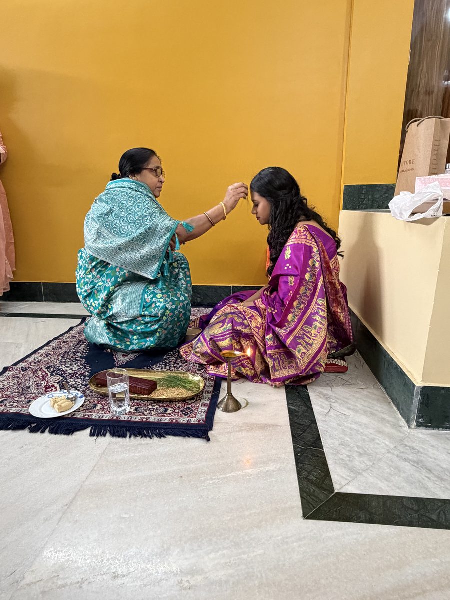 Elder woman in turquoise tenderly blessing Rituparna on the floor