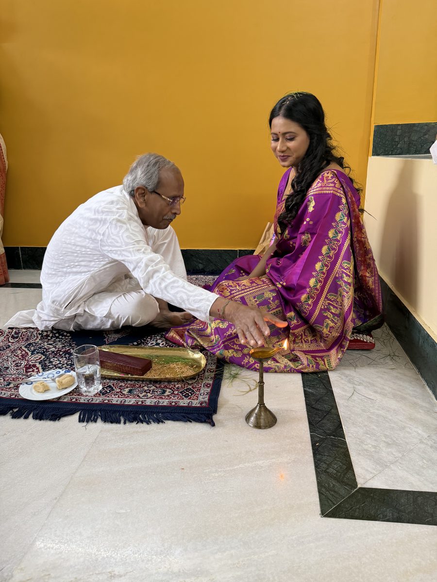 Elder man in white blessing Rituparna seated on the prayer mat